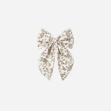 A fabric hair bow accessory featuring a delicate floral print in muted pink, olive green, and brown on a cream background, centered on a light gray studio background.