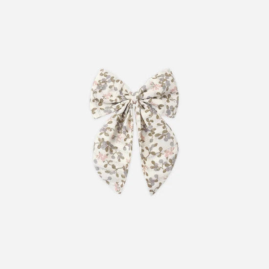 A fabric hair bow accessory featuring a delicate floral print in muted pink, olive green, and brown on a cream background, centered on a light gray studio background.