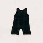 A sleeveless infant romper in a dark green and black plaid pattern, laid flat on a light beige background.