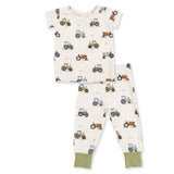 A two-piece baby pajama set featuring a short-sleeve top and matching pants. The pajamas are off-white with an all-over tractor pattern in blue, green, and orange, finished with solid sage green cuffs.