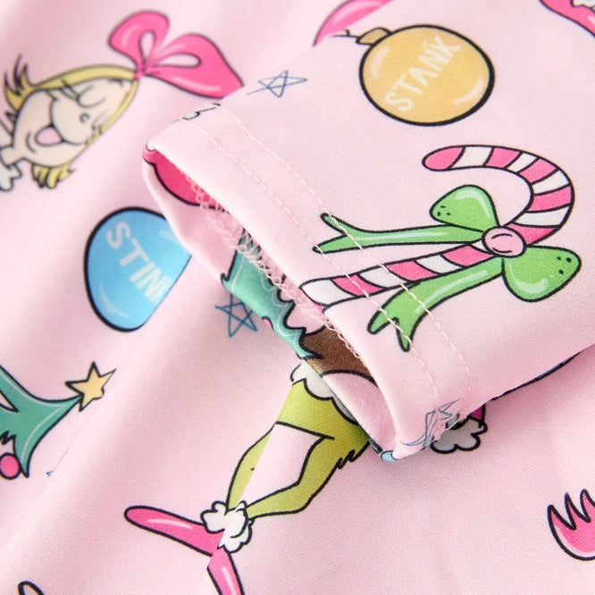 A close-up of a light pink fabric product, likely a pajama or long-sleeve top, featuring a colorful cartoon print of characters, candy canes, ornaments, and stars.