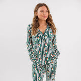 A woman modeling a matching two-piece pajama set with a green and white vertical stripe pattern with Santa faces on it, set against a plain white studio background.