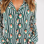 A person wearing a long-sleeve pajama set with dark green and white vertical stripes and an allover Santa Claus face print, shown against a plain light background.