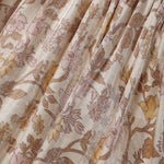 A close-up of a pleated fabric with a floral pattern in dusty pink, mustard yellow, and brown on a warm beige background.