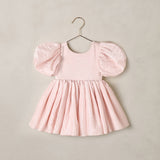 A light pink toddler dress with voluminous puff sleeves and a gathered skirt, hanging on a metal hanger against a neutral beige wall.