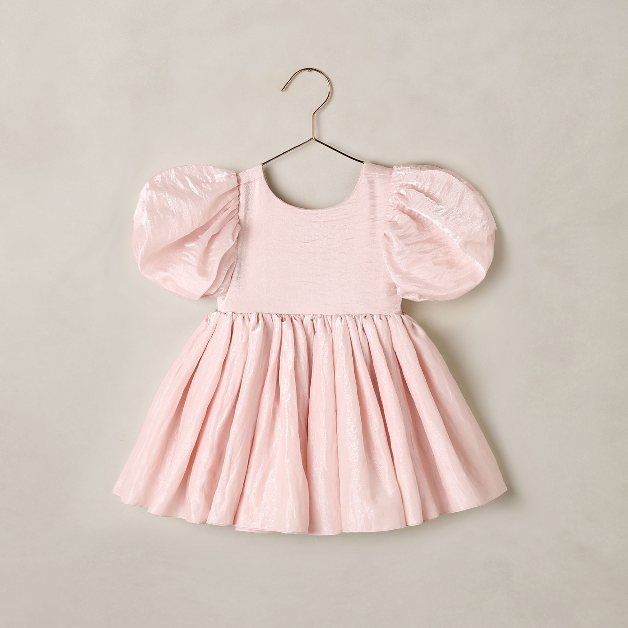 A light pink toddler dress with voluminous puff sleeves and a gathered skirt, hanging on a metal hanger against a neutral beige wall.