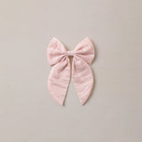 A light pink bow with a crinkled texture, centered on a solid light beige background.