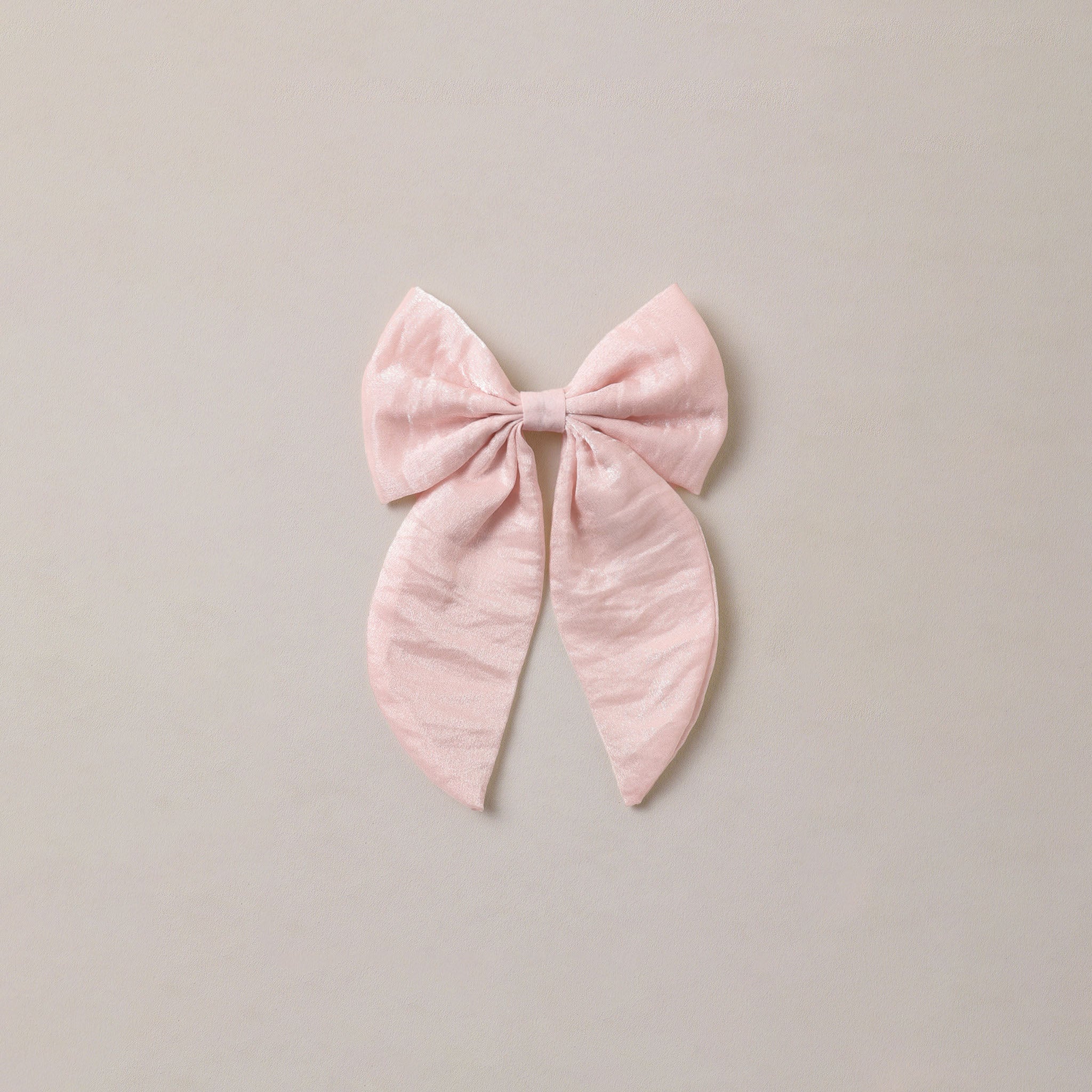 A light pink bow with a crinkled texture, centered on a solid light beige background.