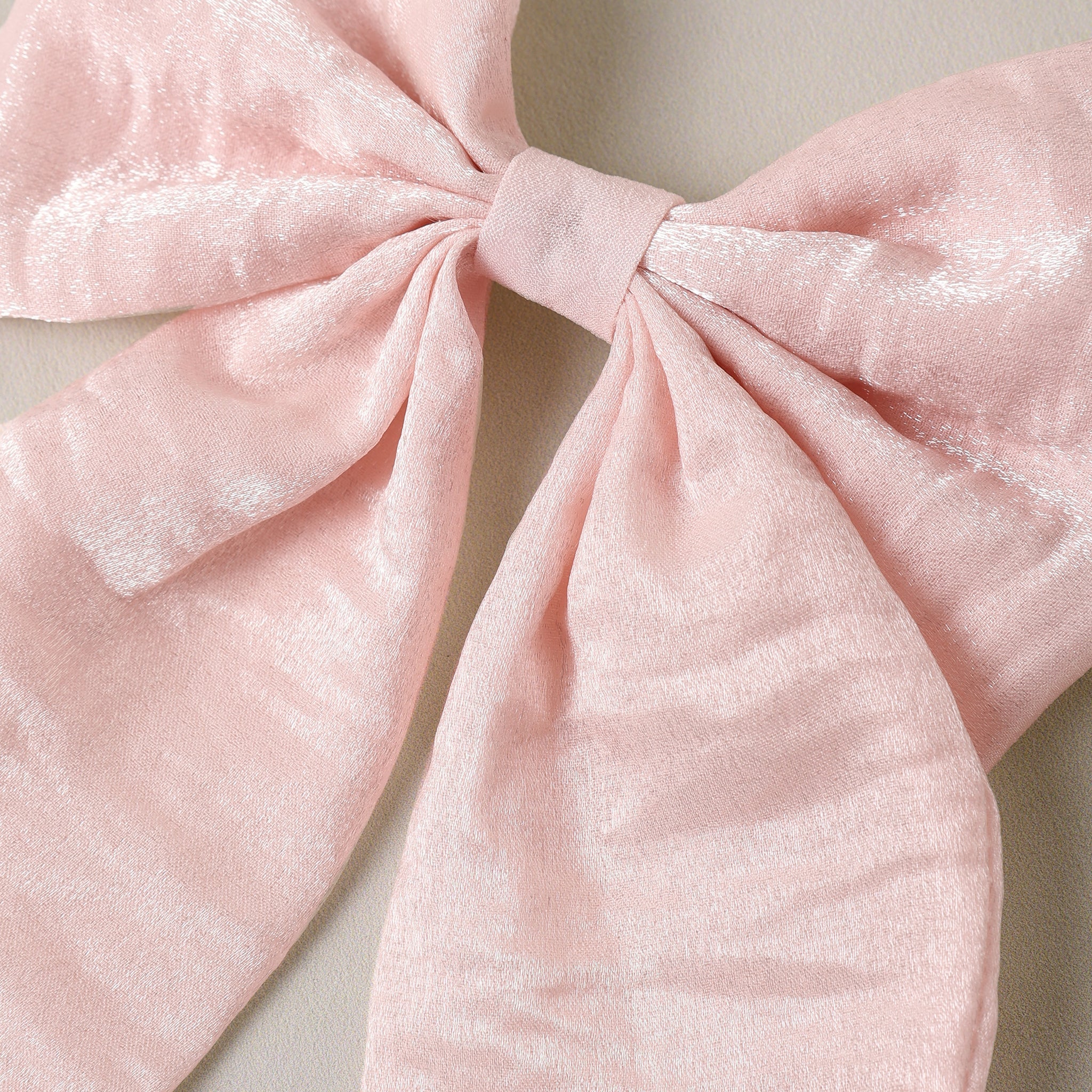 A close-up of a large light pink bow made from a soft, slightly textured fabric, set against a neutral beige background.