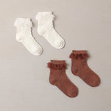 A pair of white and a pair of cinammon colored socks lay atop a gray background. 