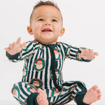 A baby sitting on a white studio background wearing a festive green and white striped one-piece pajama with Santa Claus illustrations.