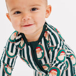 A baby crawling on a white studio floor wearing a green and white striped long-sleeve pajama with a Santa Claus print.