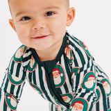 A baby crawling on a white studio floor wearing a green and white striped long-sleeve pajama with a Santa Claus print.