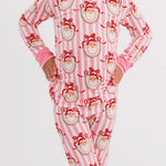 A child wearing a pink and white striped long-sleeve pajama set with a red Santa Claus face print, standing against a light gray studio background.