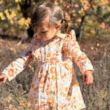 Young girl in a floral dress standing in a natural setting with trees and shrubs.