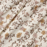 A close-up of a cream-colored fabric with a delicate floral vine pattern in muted brown, dusty pink, and mustard yellow.
