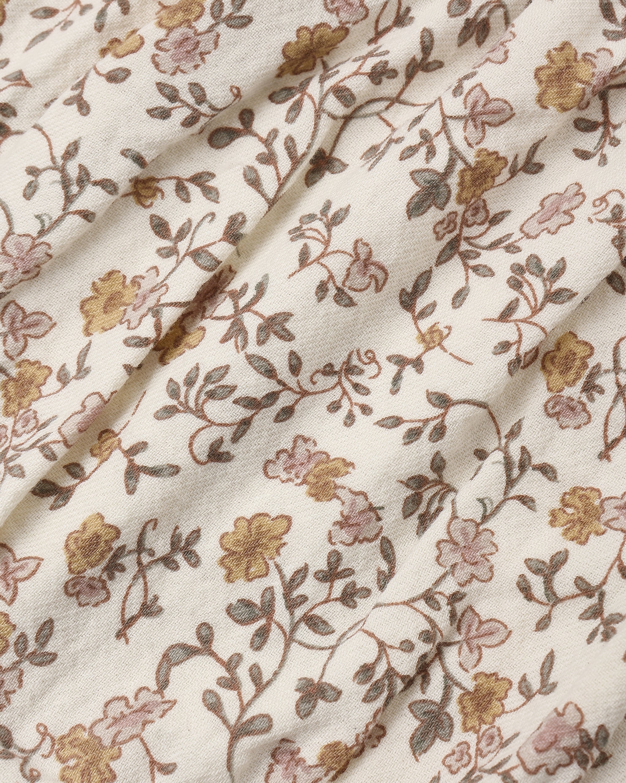 A close-up of a cream-colored fabric with a delicate floral vine pattern in muted brown, dusty pink, and mustard yellow.