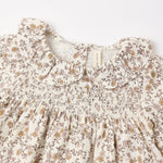 Close-up of a cream-colored children's dress with a brown and muted yellow floral print, featuring a smocked bodice and ruffled collar.