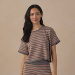 A woman modeling a matching two-piece knit loungewear set featuring a short-sleeve top and leggings with horizontal brown, beige, and gray stripes, set against a solid beige background.