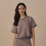 A woman modeling a matching two-piece knit loungewear set featuring a short-sleeve top and leggings with horizontal brown, beige, and gray stripes, set against a solid beige background.