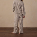 A person standing with their back to the camera wearing a matching two-piece pajama set with a beige and brown animal print pattern, set against a neutral beige wall and dark wood floor.