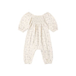A baby romper in a warm cream or off-white color with a delicate, small-scale floral print in muted blue and green. The romper features a smocked bodice, short puff sleeves, and leg openings that are gathered together at the ankles.