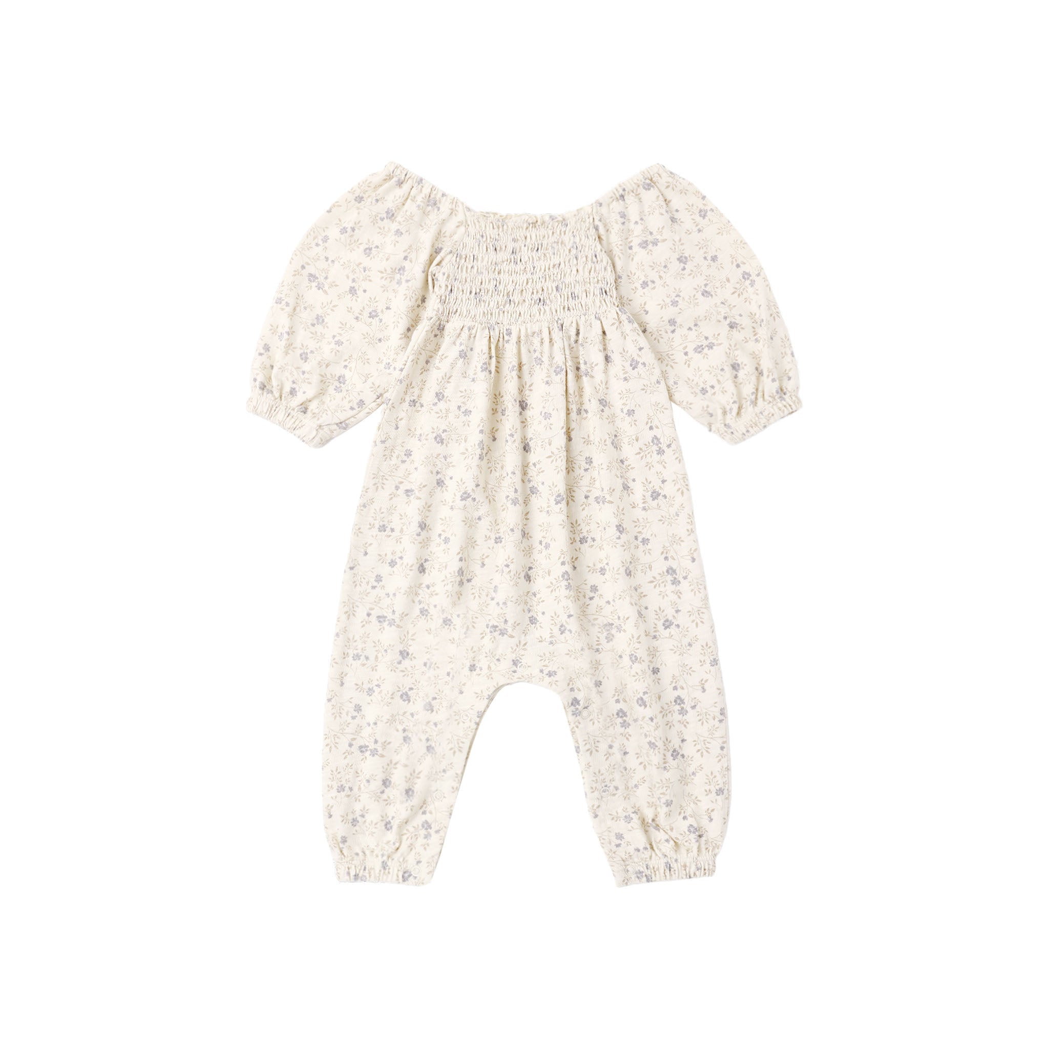 A baby romper in a warm cream or off-white color with a delicate, small-scale floral print in muted blue and green. The romper features a smocked bodice, short puff sleeves, and leg openings that are gathered together at the ankles.
