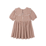 A toddler girl's short-sleeve dress with a brown and white gingham pattern, featuring a large Peter Pan collar with white lace trim, a buttoned front, and a gathered flared skirt.