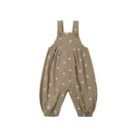A pair of toddler's overall-style romper pants in a warm taupe-brown color, decorated with a small white floral pattern, shown against a plain white background.