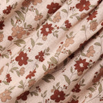 A close-up of draped fabric with a delicate floral print on a warm beige background. The pattern features muted red-brown flowers, soft peach blossoms, and olive-green leaves.