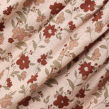 A close-up of draped fabric with a delicate floral print on a warm beige background. The pattern features muted red-brown flowers, soft peach blossoms, and olive-green leaves.