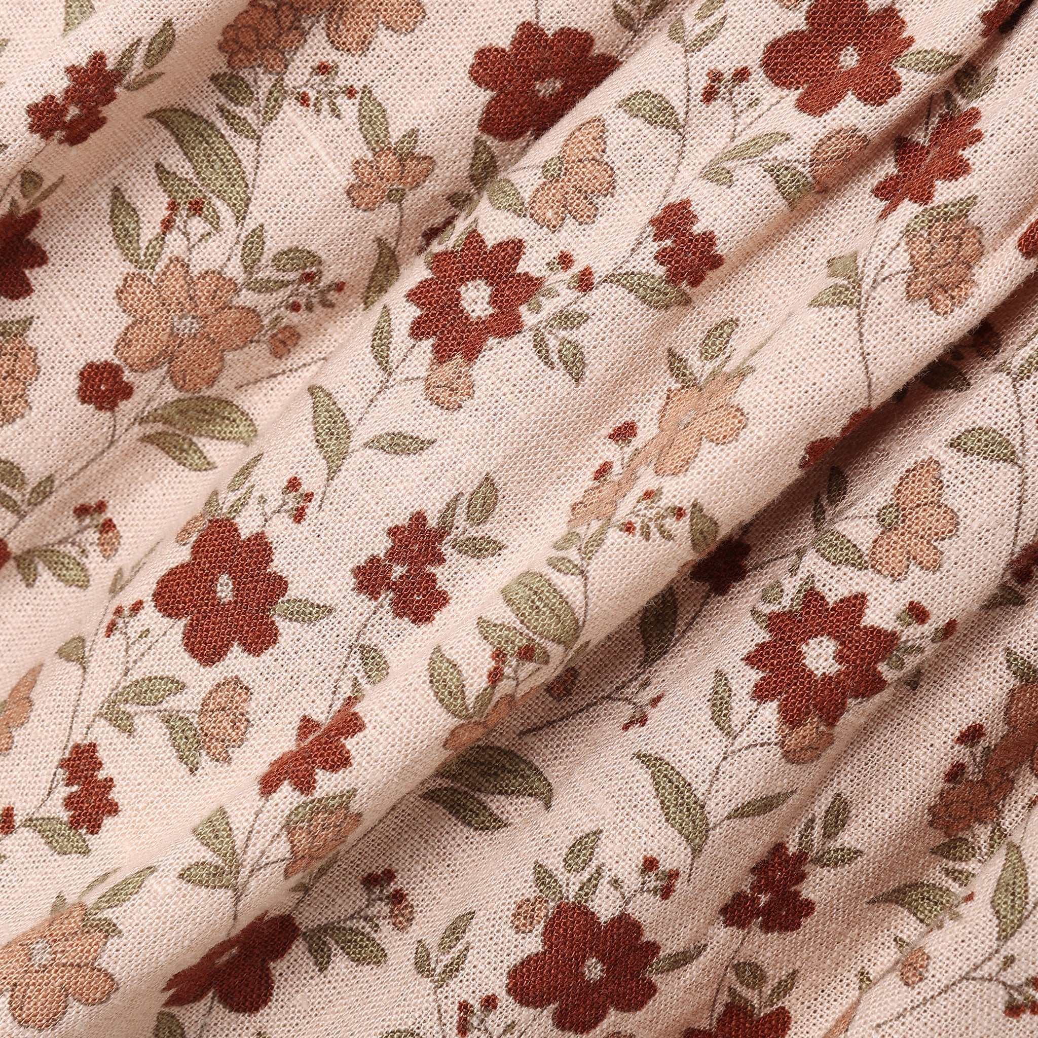 A close-up of draped fabric with a delicate floral print on a warm beige background. The pattern features muted red-brown flowers, soft peach blossoms, and olive-green leaves.