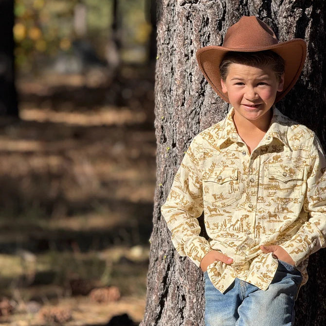 Child wearing a cowboy hat and patterned shirt leaning against a tree in a natural setting