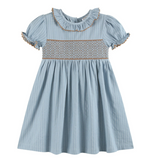 A light blue and white vertically striped cotton dress for toddlers, featuring a smocked chest panel with a tan geometric pattern, a ruffled collar, and short puff sleeves with ruffled trim.
