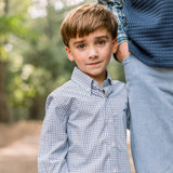 Young boy wearing a checkered shirt standing outdoors with a blurred background