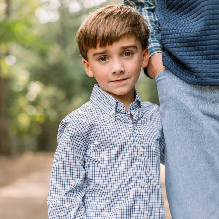 Young boy wearing a checkered shirt standing outdoors with a blurred background