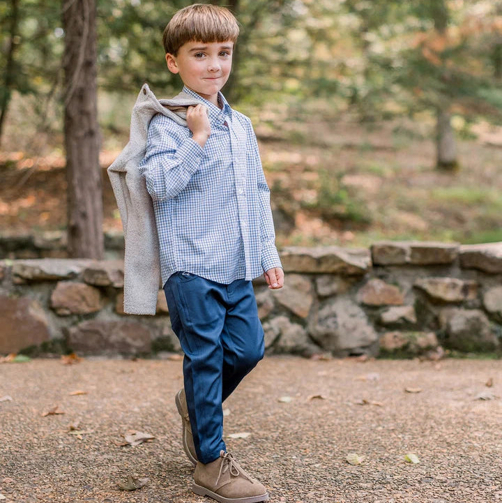 Young boy standing outdoors with a stone wall and trees in the background