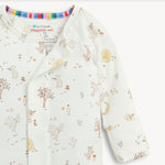 A close up of a long-sleeve baby romper by Magnetic Me in off-white, decorated with a whimsical woodland print of bears, trees, flowers, and a crescent moon.