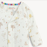 A close up of a long-sleeve baby romper by Magnetic Me in off-white, decorated with a whimsical woodland print of bears, trees, flowers, and a crescent moon.