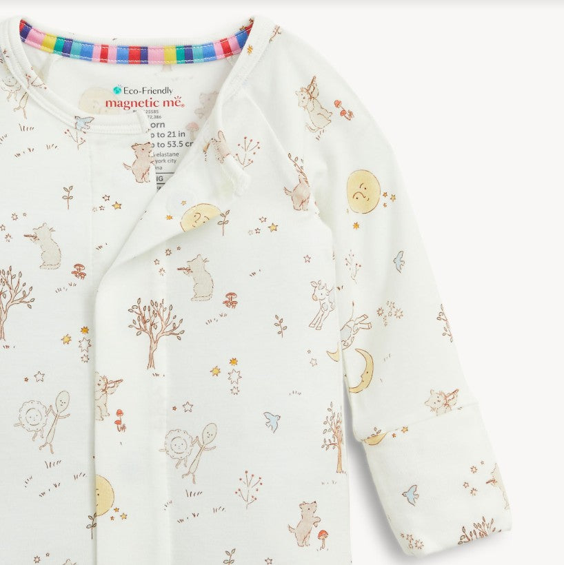 A close up of a long-sleeve baby romper by Magnetic Me in off-white, decorated with a whimsical woodland print of bears, trees, flowers, and a crescent moon.