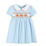 A light blue baby girl's dress with a white Peter Pan collar, short puff sleeves, and a smocked chest panel featuring three orange pumpkins and green vines.
