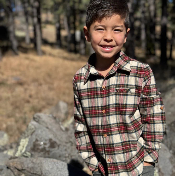 Child wearing a plaid shirt standing outdoors with trees in the background
