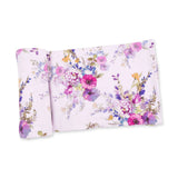 A folded blanket, featuring a colorful watercolor floral pattern with pink, purple, blue, and green tones, set against a plain white background.