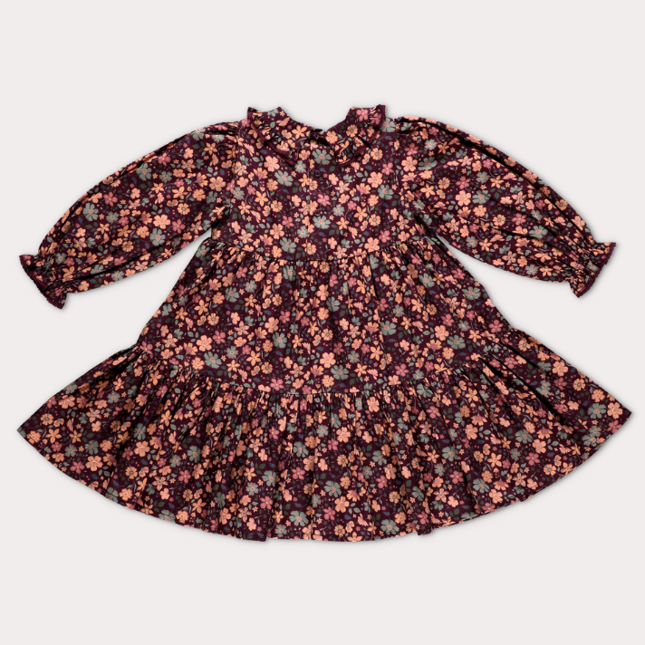 A long-sleeve baby dress with a ruffled collar and a dense floral print, laid flat on a light gray background.