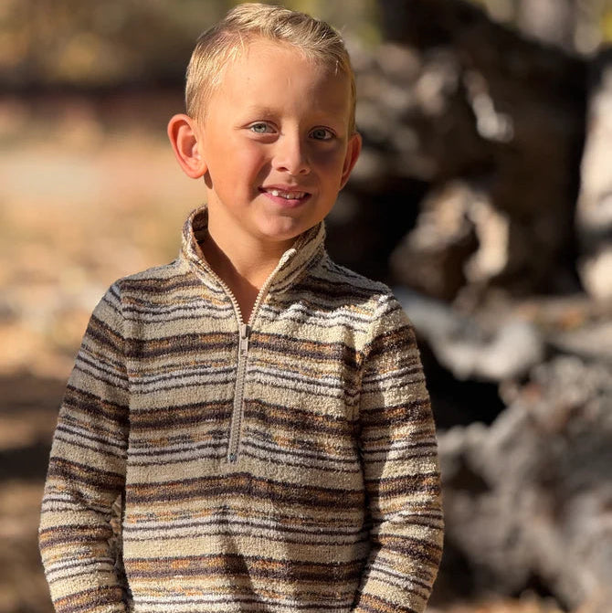 Young boy wearing a striped sweater standing outdoors with trees in the background