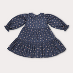 A navy blue long-sleeve baby dress with a small white and pink floral print, featuring a Peter Pan collar, ruffled cuffs, and a tiered skirt, laid flat on a light gray background.
