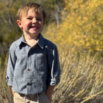 Young boy standing outdoors in a natural setting with greenery.