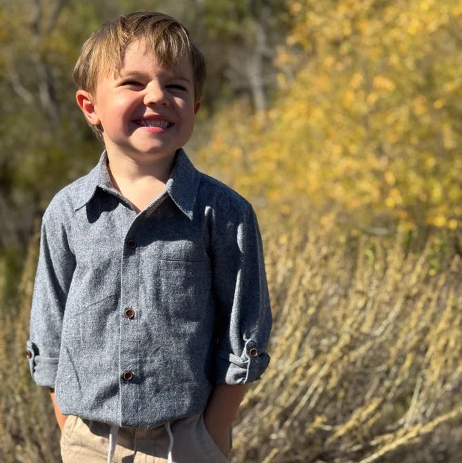 Young boy standing outdoors in a natural setting with greenery.