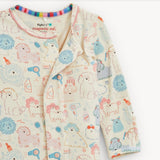 A baby long-sleeve pajama top with a playful cartoon print of sheep, lions, and other animals in pastel colors on a cream background. The brand name 'magnetic me.