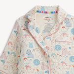 A close-up of a children's pajama top with a playful dog print. The pajamas feature a cream base color with cartoon dogs in light blue, pink, and orange, outlined in black.